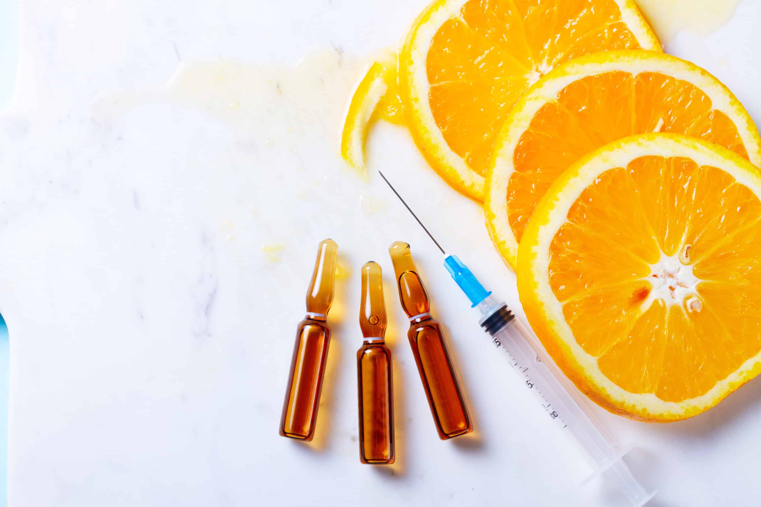 Vitamin shots laid next to slices of orange.